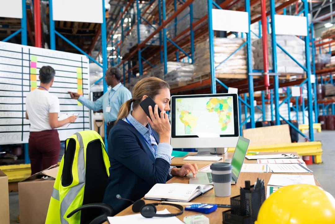 Mujer de negocios hablando por teléfono frente a una computadora con un mapa, representando la planificación de soluciones de aire acondicionado para oficinas industriales en México por Bioclimex.