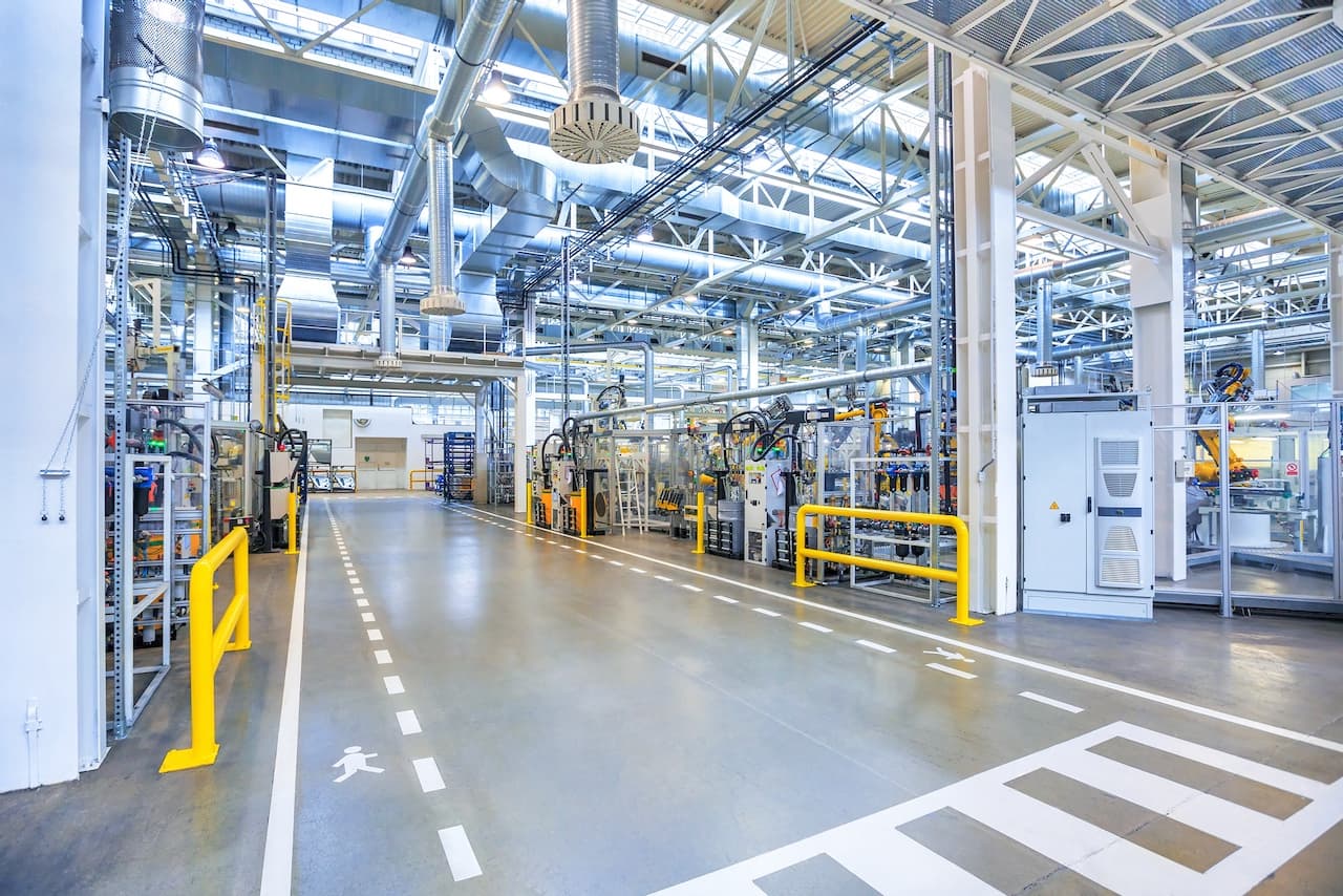 Vista interna de una fábrica moderna con iluminación brillante y pasillos despejados, mostrando cómo Bioclimex mantiene un entorno seguro y bien ventilado.