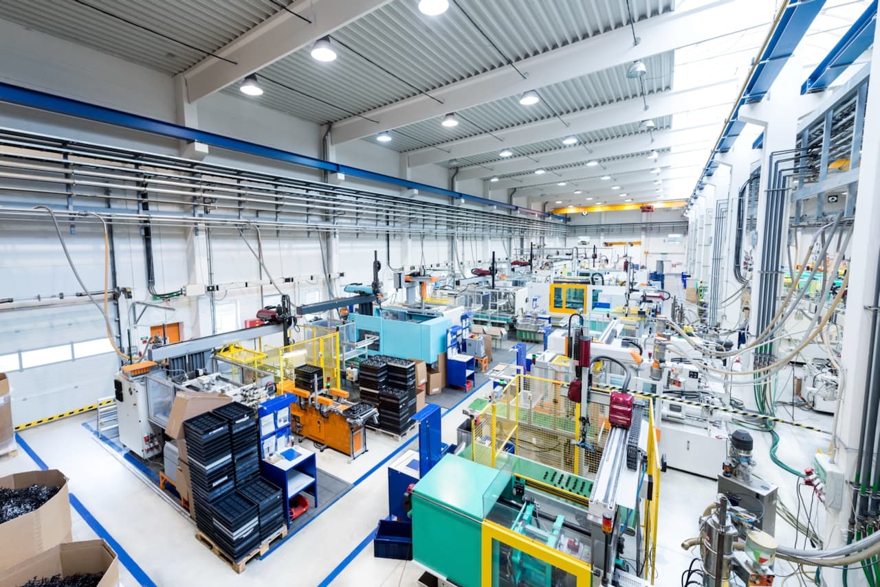 Interior de una planta de ensamblaje con varias estaciones de trabajo y empleados, destacando cómo Bioclimex mantiene la ventilación en operaciones industriales.