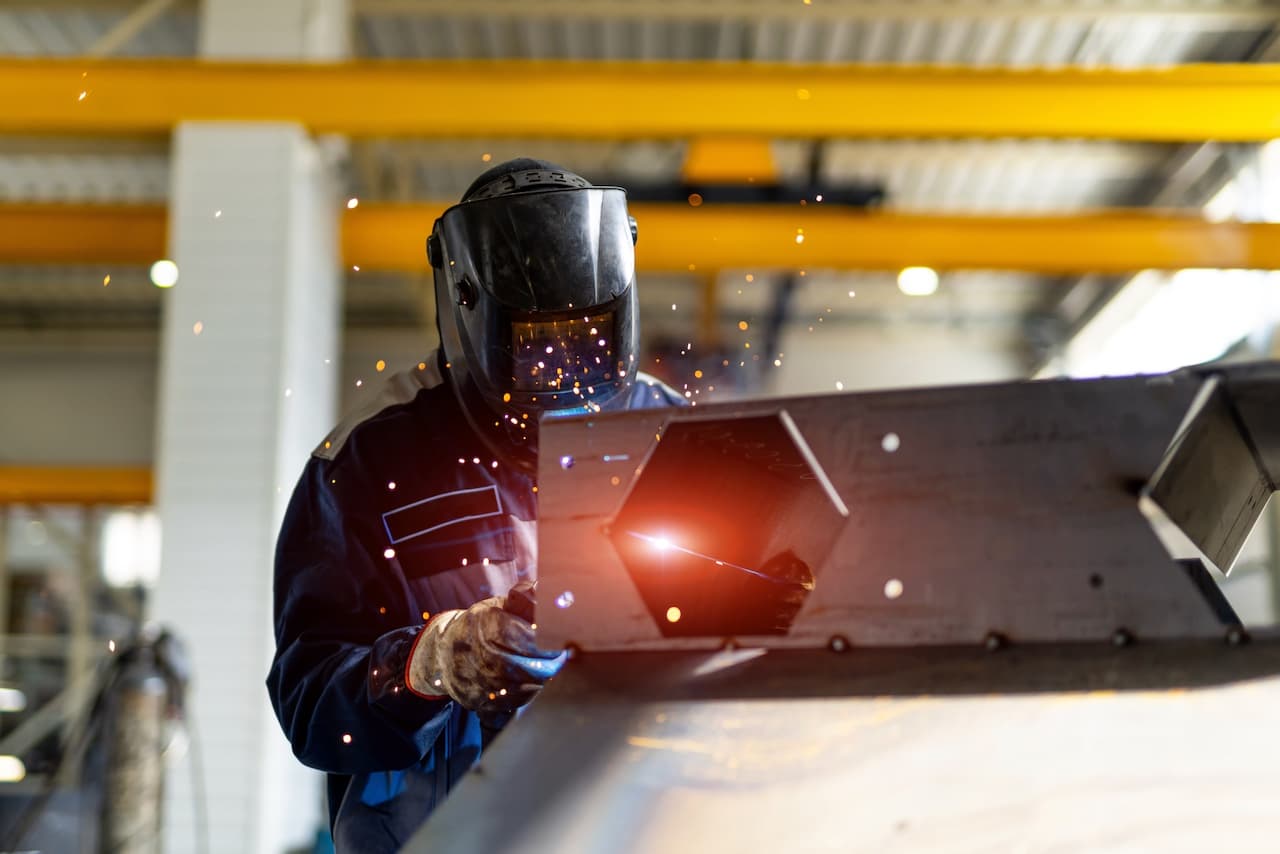 Soldador en acción con chispas volando, trabajando en un entorno industrial donde Bioclimex asegura una ventilación adecuada para la seguridad del trabajador.
